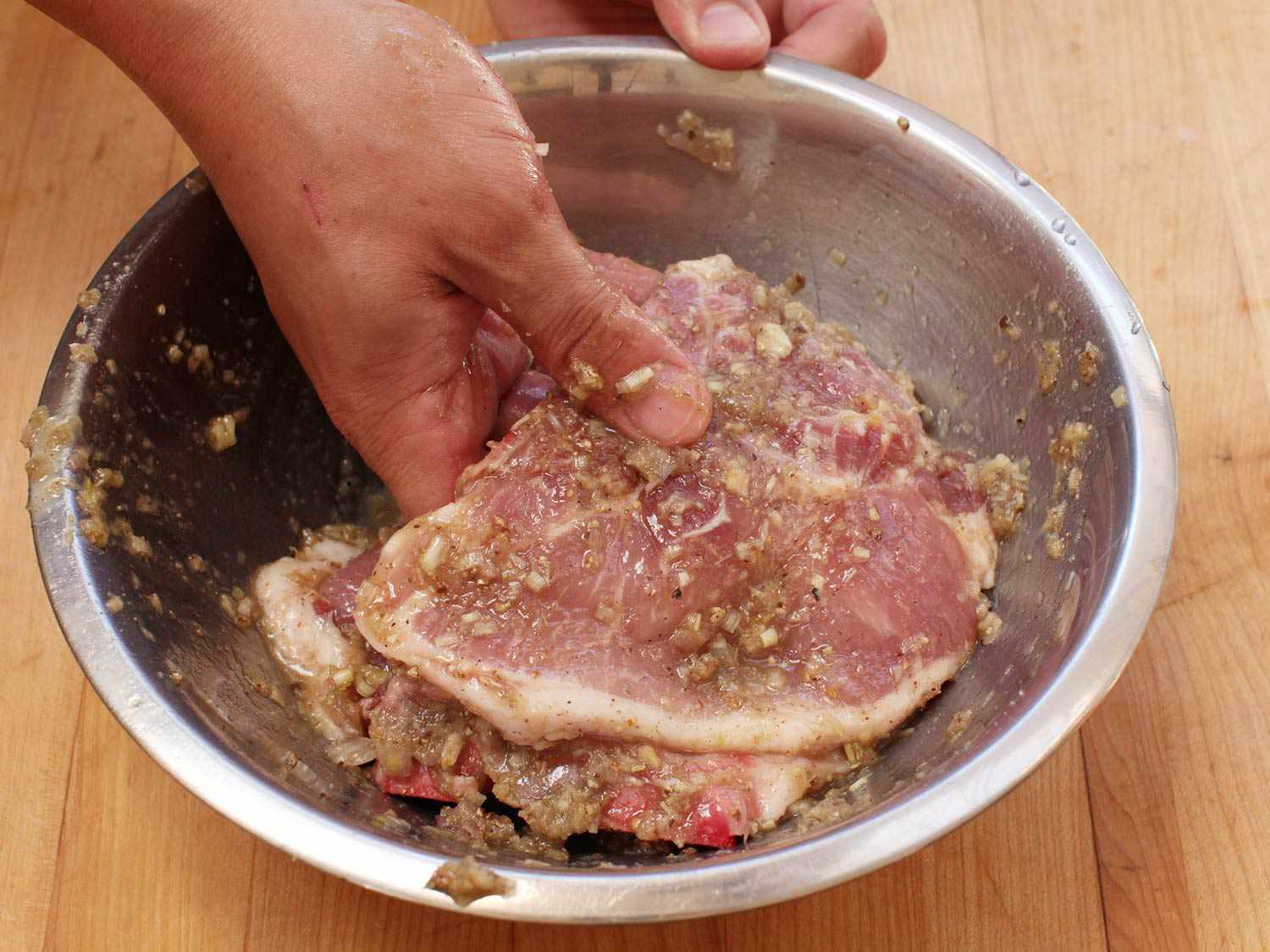 Adding thinly sliced pork chops to marinade in metal bowl for Vietnamese lemongrass grilled pork chops.