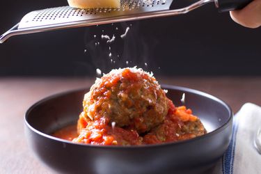 把帕玛森干酪放在意大利美式肉丸上，用红酱汁放在一个深色的碗里。