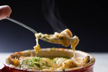 用勺子从红碗里舀出一口芝士法式洋葱汤。