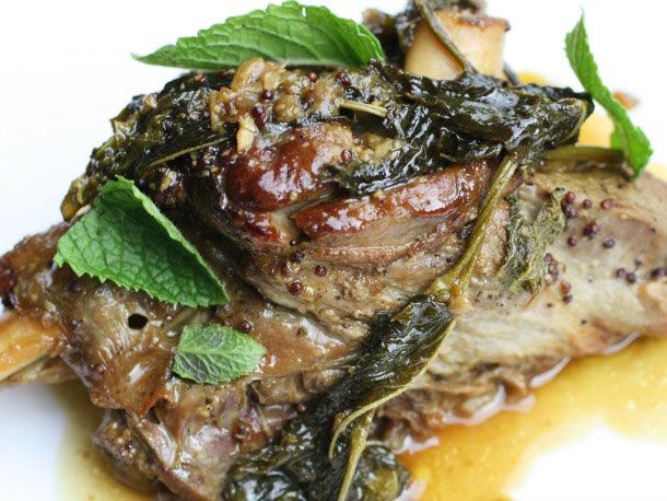 Closeup of braised lamb shank with mustard and fresh mint leaves.