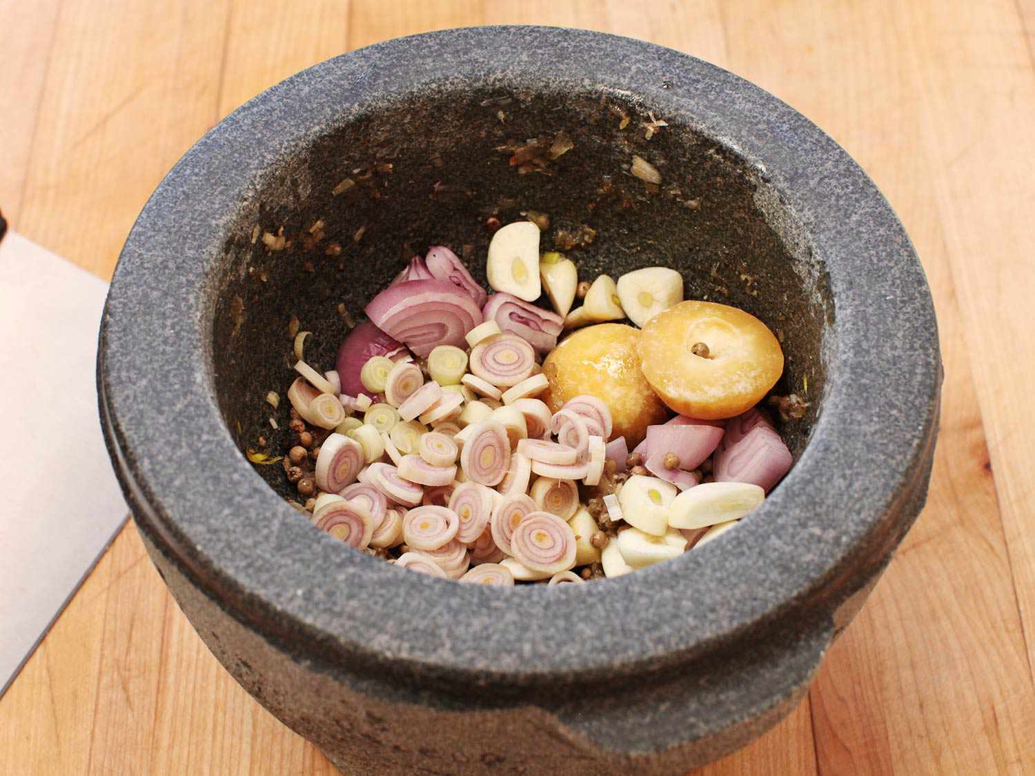 Lemongrass, shallots, garlic, palm sugar, and spices in stone mortar to pound for pork chop marinade.