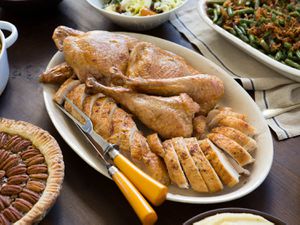 一盘用刀叉雕刻的火鸡，周围是山核桃派，青豆砂锅和沙拉