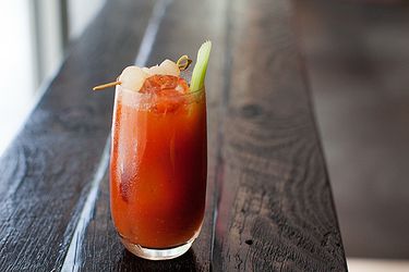 A Bloody Mary cocktail in a tall glass garnished with a celery stick and some shrimp on a toothpick.