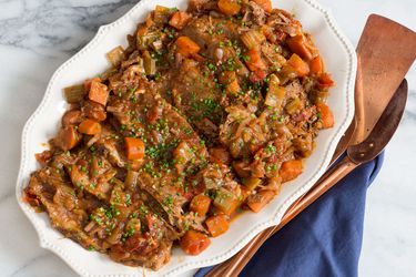 Platter of Jewish-style braised brisket with carrots and onions, topped with chives.