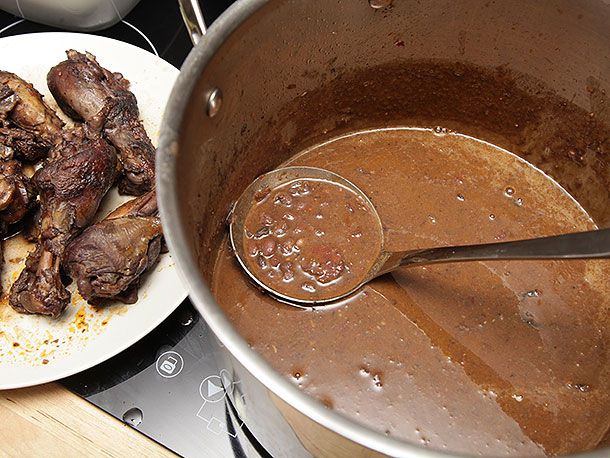 用勺子从高汤锅里舀出豆汤。背景是盘子里的红烧鸡。