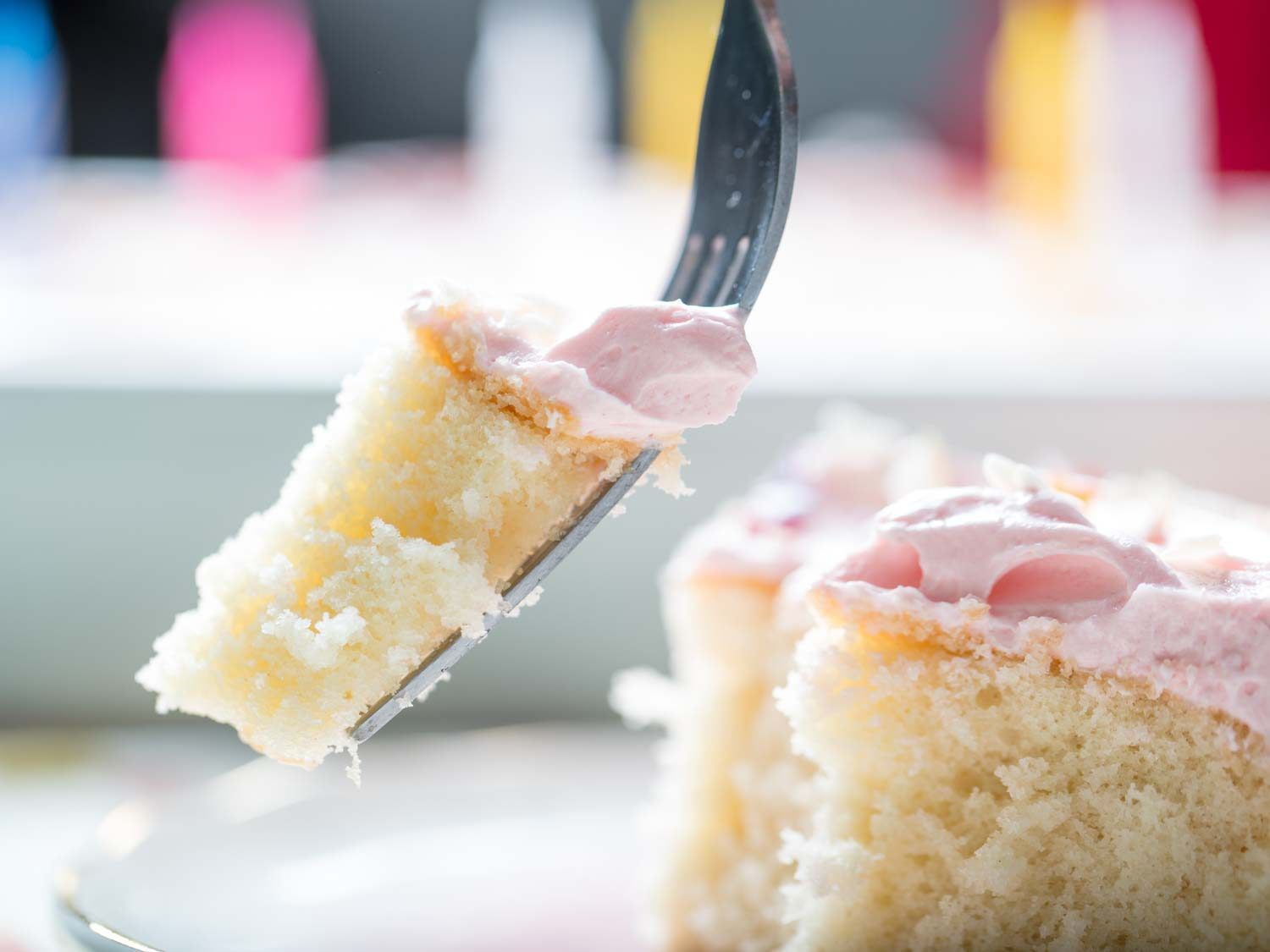 用叉子叉着一块黄色蛋糕，上面有粉红色的香草奶油糖霜。gydF4y2Ba
