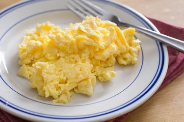 A white and blue plate with a pile of fluffy scrambled eggs and a fork.