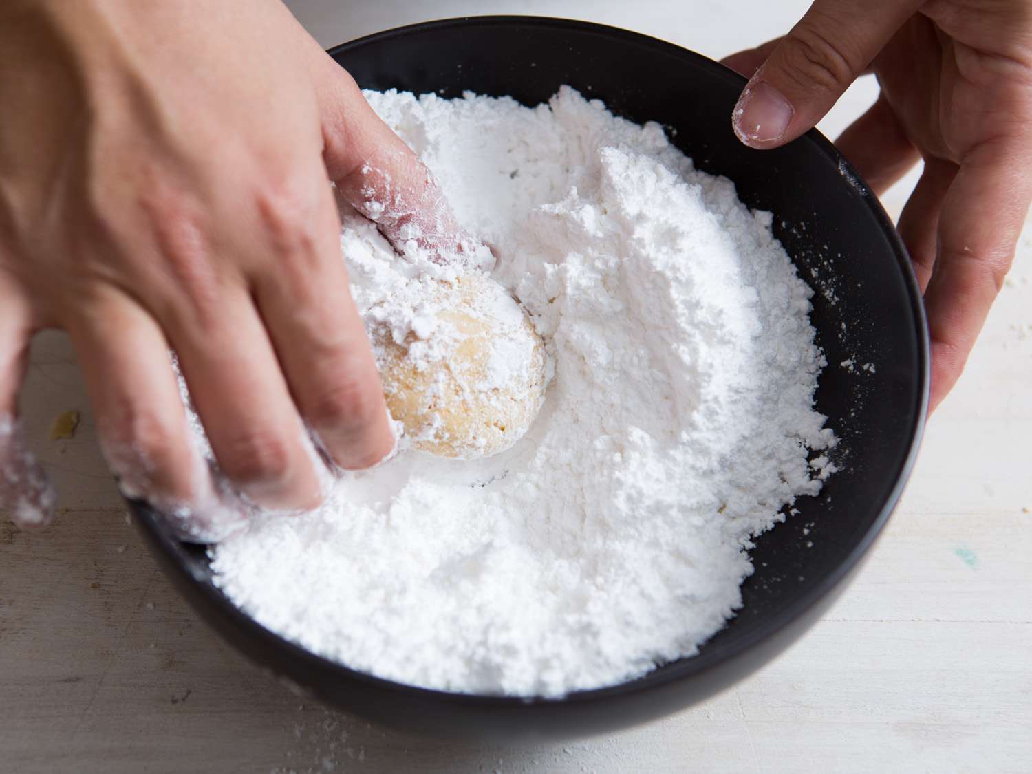 把烤好的雪球饼干放在一小碗糖粉里滚动