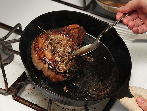 Basting a seared pork chop topped with shallots and thyme in cast iron skillet