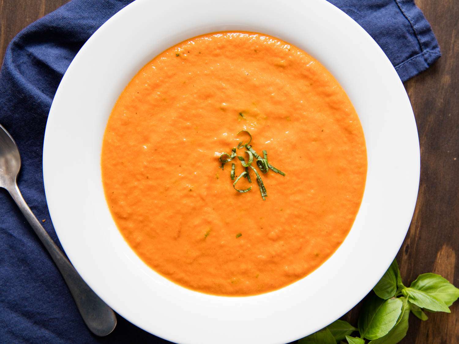 Overhead shot of bowl of thick, creamy tomato soup garnished with basil