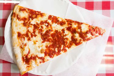 A slice of New York pizza on a paper plate.