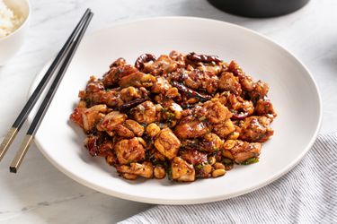A plate of real-deal kung pao chicken with chopsticks on the side of the plate.