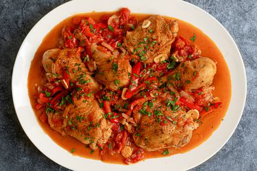 A white oval platter holding chicken cacciatore and a good amount of golden brown sauce. The platter is on a textured grey-blue surface.