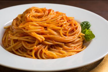 A serving of spaghetti that has been lightly coated with tomato sauce and fashioned into a swirl-like heap in a shallow bowl.